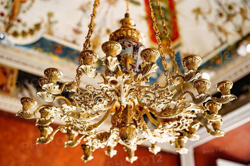 Close-up of an antique gold Italian chandelier. A chandelier-chandelier on gilded chains hangs against the background of the painted ceiling.