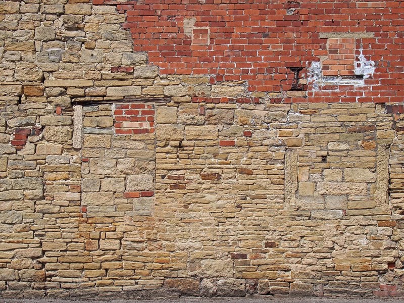 An old exterior wall with an irregular patched and repaired brick and stone surface
