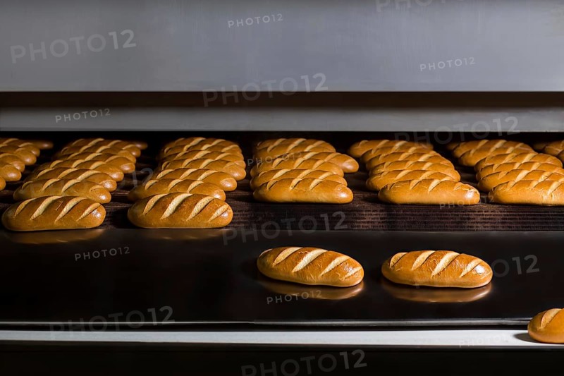 Baguettes baking in industrial oven. Loaves of bread at production line. Food factory