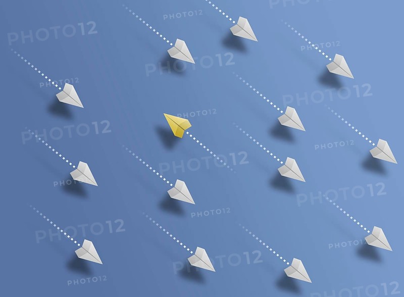 group of paper planes flying in one direction on blue background and one paper glider going in different or opposite direction, breaking new ground and stepping out of the line concept