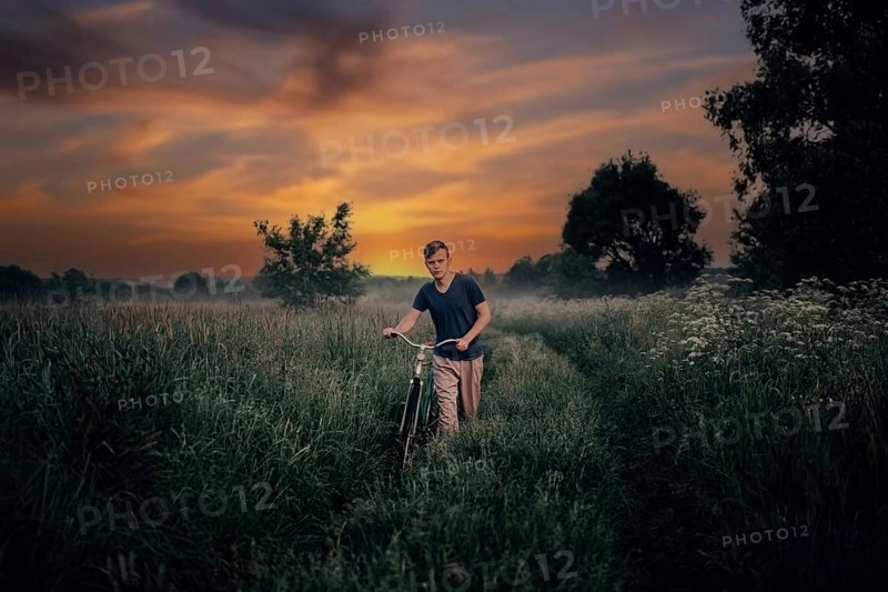Young man walks with a retro bike along a field road, vintage style in the village at sunset. Sadness and romance in nature