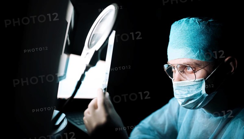 A doctor intensely examining a sample using a magnifying glass in a dimly lit room