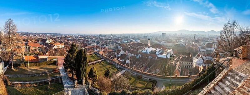 Wide panorama of Graz City, City rooftops, Mur river and city center, Schlossberg hill and clock tower Sun in winter, blue sky. Travel destination