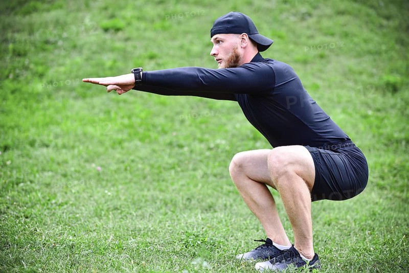 Full length of young concentrated sportsman doing squats outdoors