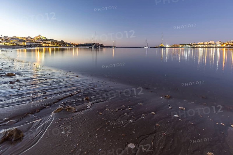 Night shot of a sandy beach and harbour at low tide. Panoramic image of an illuminated historic city centre at dawn in Ferragudo, Portimão, Algarve, Portugal, Europe