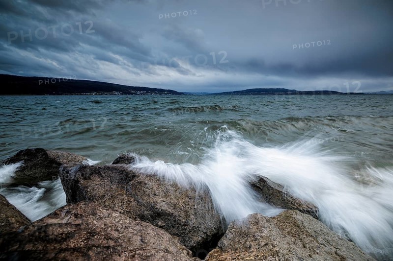 Sprayed waves crash against stones in front of a cloudy sky, harbour, Mittelzell, Reichenau, Lake Constance, Baden-Württemberg, Germany, Europe
