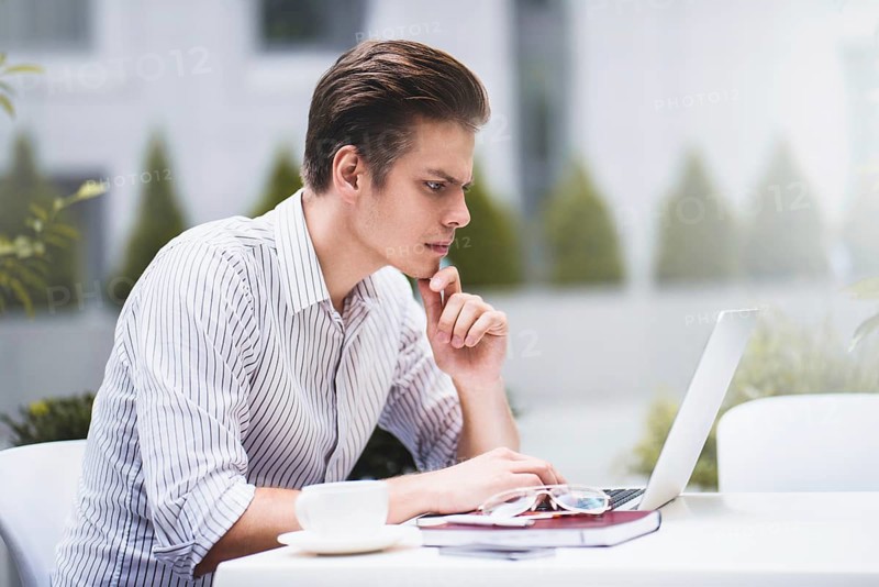 Smart attitude. Positive handsome man using a laptop and sitting in the cafe while surfing the internet