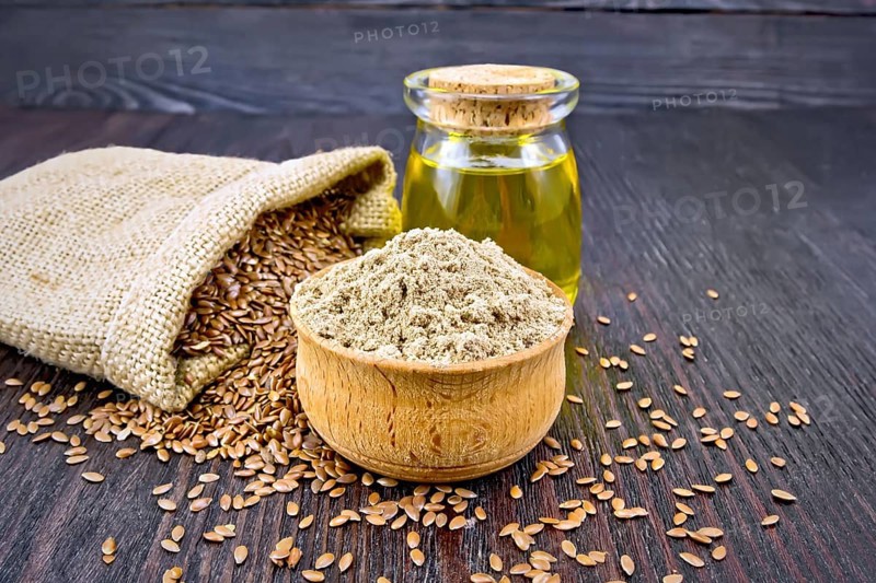 Flax flour in a bowl, seeds in a bag and on a table, linseed oil in a glass jar on a wooden board background
