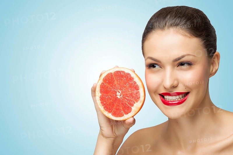 A creative portrait of a beautiful girl holding a red grapefruit sexually under her chin