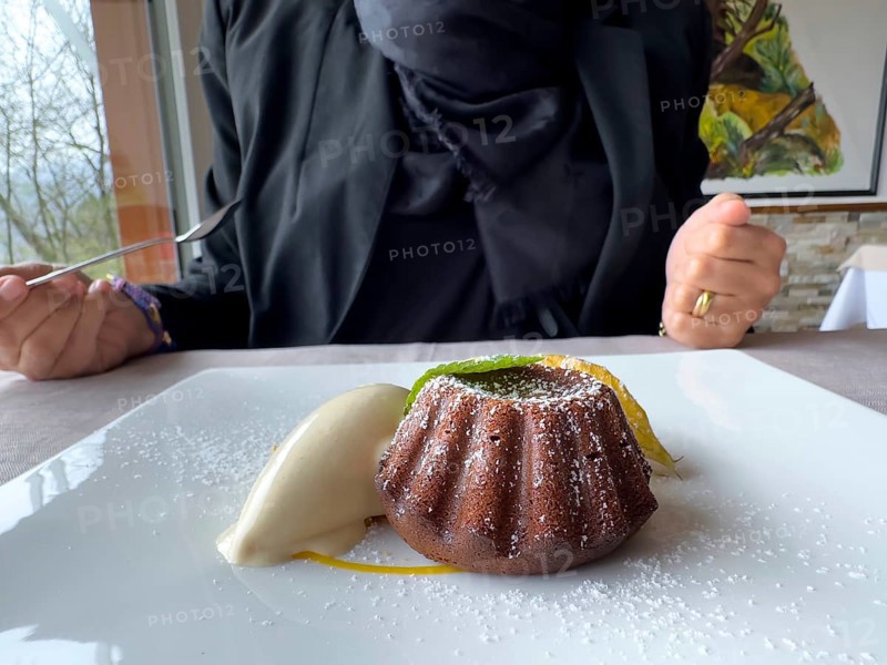 Woman Eating on a White Plate With an Elegant Warm Dark Chocolate Cake Dessert With Vanilla Ice Cream and one Mint Leaf in Switzerland.