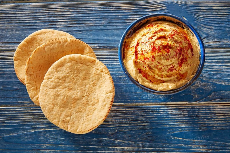 Hummus with pita bread and red pepper powder on blue Mediterranean wood table