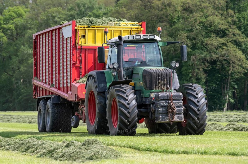 Picking up dried grass for silage with a green tractor and red loader wagon