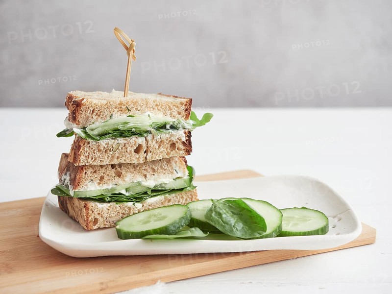 Cucumber and green spinach sandwich, cut in half and stacked on white platter