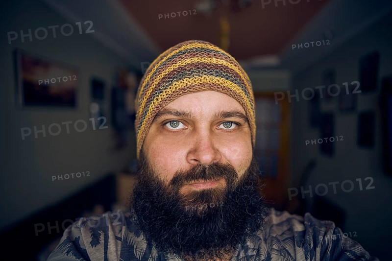 A man with a beard wearing a striped hat and shirt, looking up into the camera