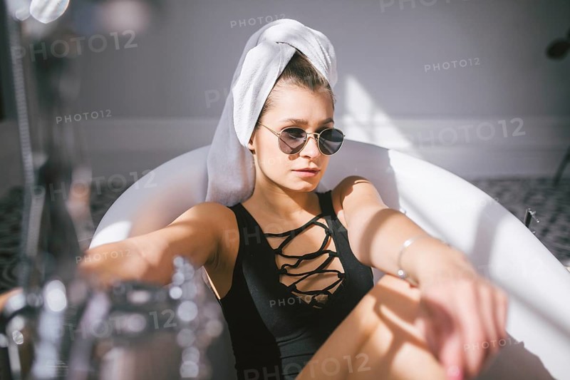 Young caucasian woman with towel on head and sunglasses getting spa treatment in a beauty salon, inside an interior room. Relaxing in the bathroom in linen. The concept of body care and relaxation