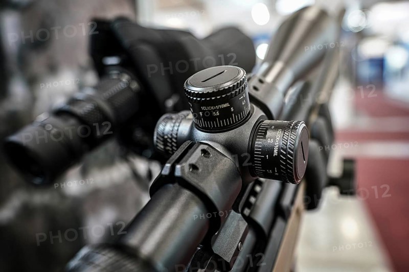 Black shooting scope optics mounted on rifle displayed at weapons exhibition fair, closeup detail to adjustment knobs