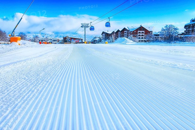 Close-up groomed snow at Bansko resort, Bulgaria panorama with ski slope and cable car lift