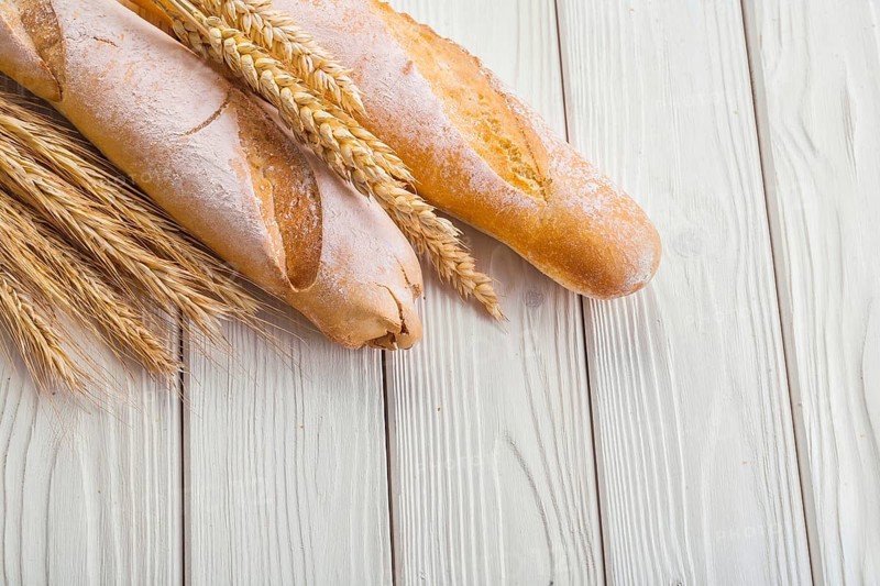Two baguettes and ears of wheat on old white wooden boards with copyspace