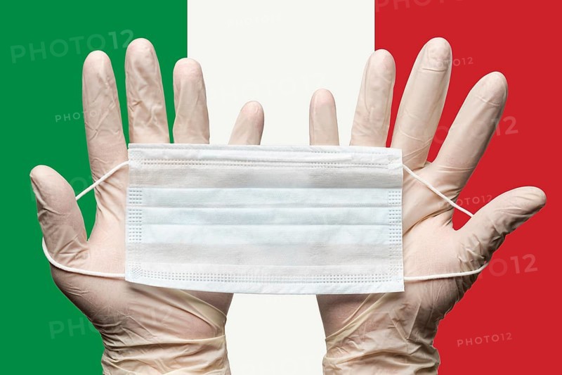 Paramedic holding respiratory face mask in two hands in white gloves on background flag of Italy. Concept coronavirus quarantine, pandemic outbreak, grippe. Medical respiratory bandage for face