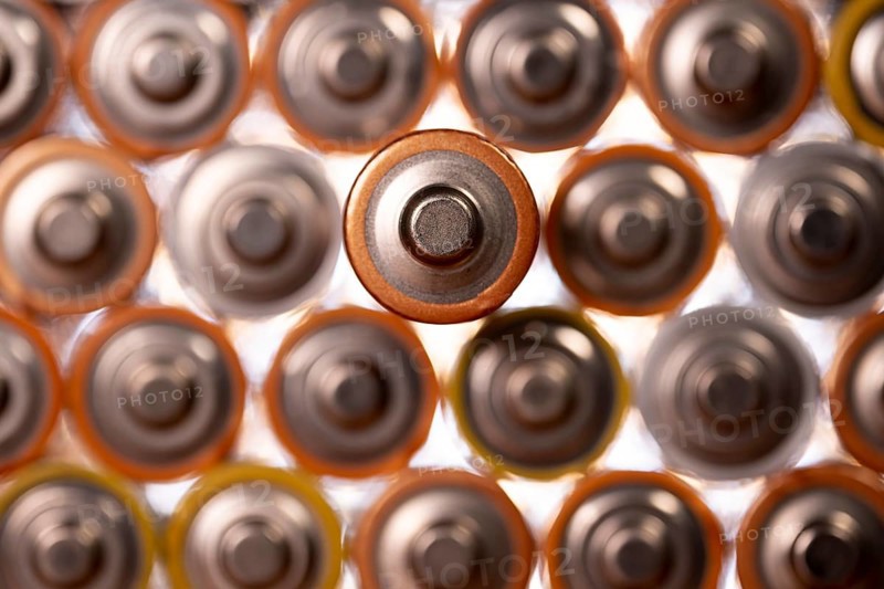 Multiple used AA alkaline batteries are seen arranged in a pile. Closeup front view from the plus side of the battery
