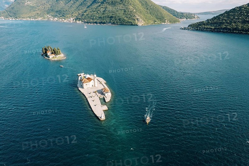 Motor boat sails on the sea past the island of Gospa od Skrpjela. Montenegro. Drone.