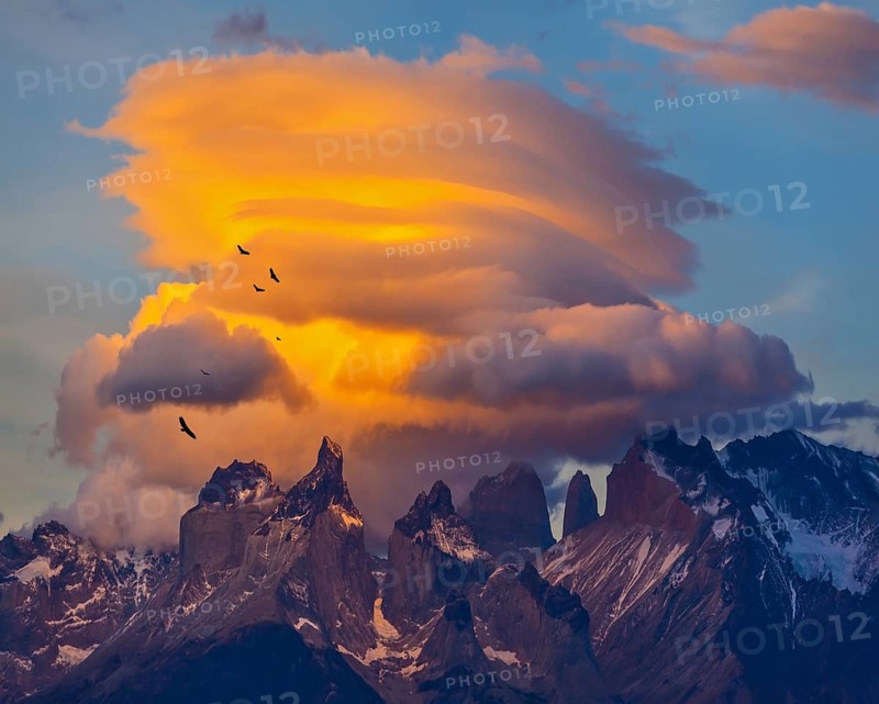 Sunset in the national park Torres del Paine, Chile. Sharp curved peaks Los Quernos. Under the clouds flying flock of Andean condors
