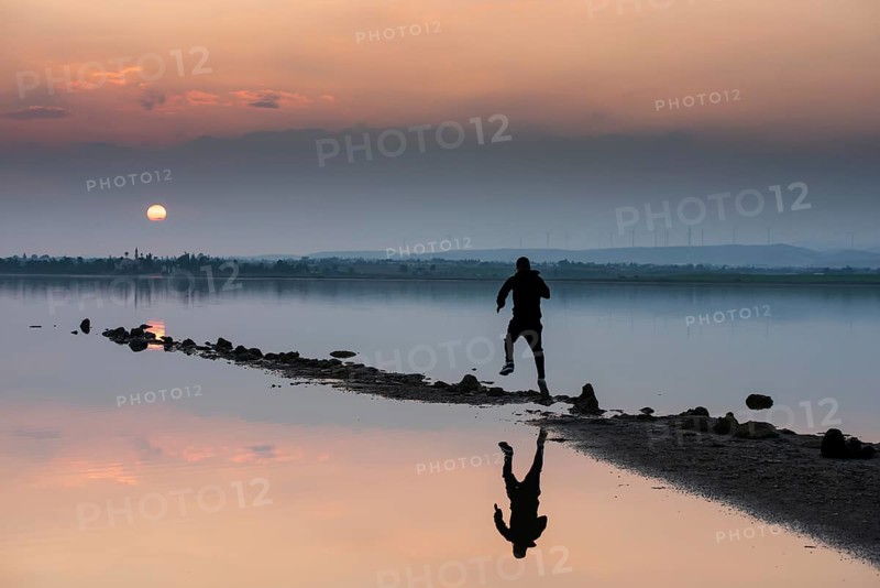 Unrecognised person running to reach the sun. Idyllic winter sunset at a lake. Silhouette reflection on water, Larnaca Cyprus