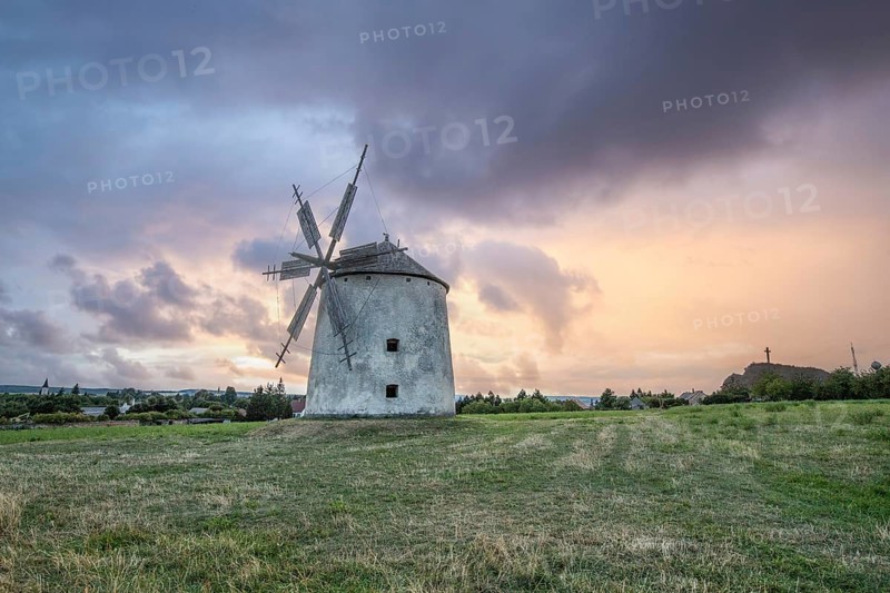 Windmill with wooden sails in a landscape with fields. Meadows and flowers appear in the sunset. Landscape shot in nature with a windmill. Historically atypical for the Balaton region in Hungary