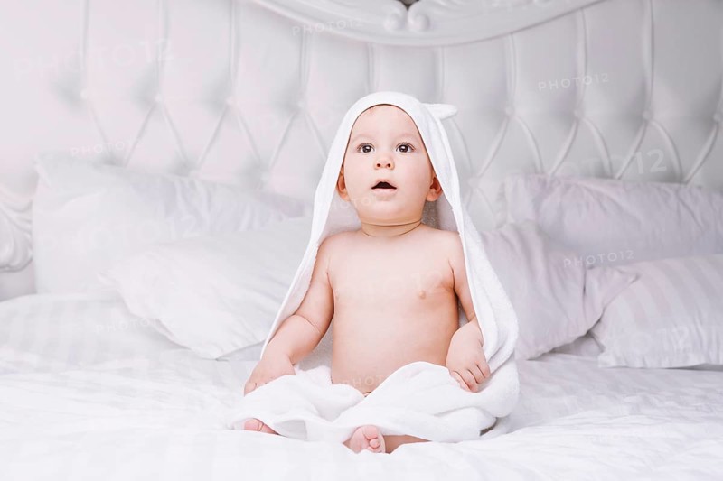Adorable newborn baby boy with brown eyes sitting wrapped in a white towel with ears in light bed. A happy childhood and the concept of health. Joyful, happy, emotional. beautiful baby