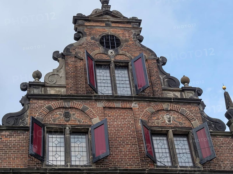 Historic brick façade with decorative elements and red shutters against a cloudy sky, nijmegen, the netherlands