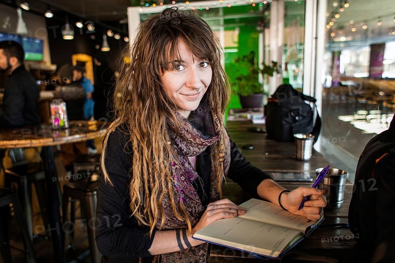 Portrait of smiling beautiful girl with dreadlocks and tattoos. Writing on a notebook with a pen in her hand. Selective focus with blurred background