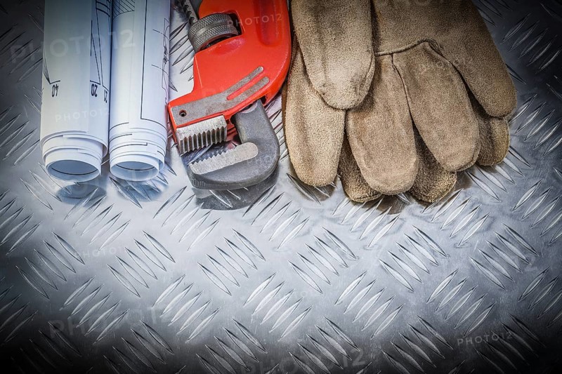 Pipe wrench construction plans leather safety gloves on corrugated metal background building concept