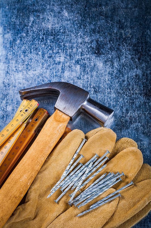 Leather safety working gloves set of construction nails wooden meter and claw hammer on scratched metallic surface building concept