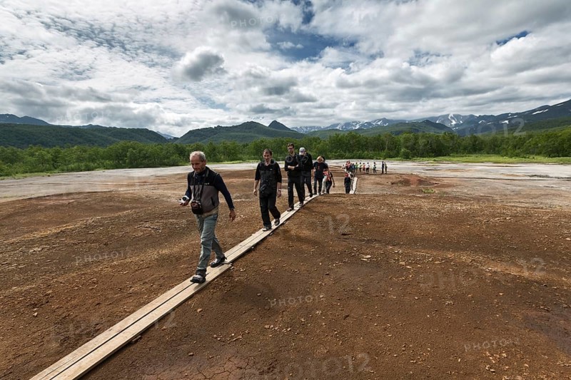 NALYCHEVO, KAMCHATKA, RUSSIA, JULY 30, 2014: Tourists walk on wooden deck, overlooking Thermal Pad Boiler, or Travertine Shield Boiler, with sleep and active griffins (mud pot) with thermal water