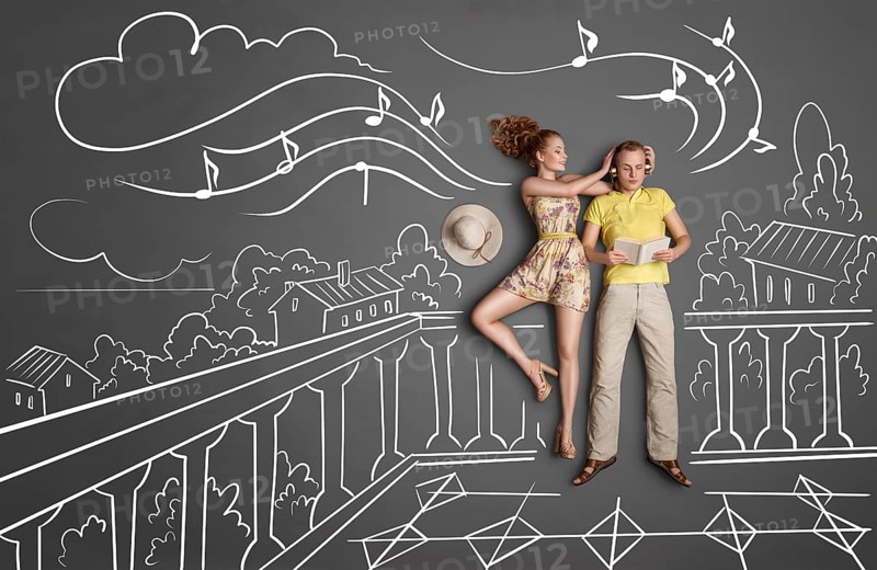 Love story concept of a romantic couple with different interests on holiday against chalk drawings background. Male listening to music in headphones and reading a book, female trying to attract his attention