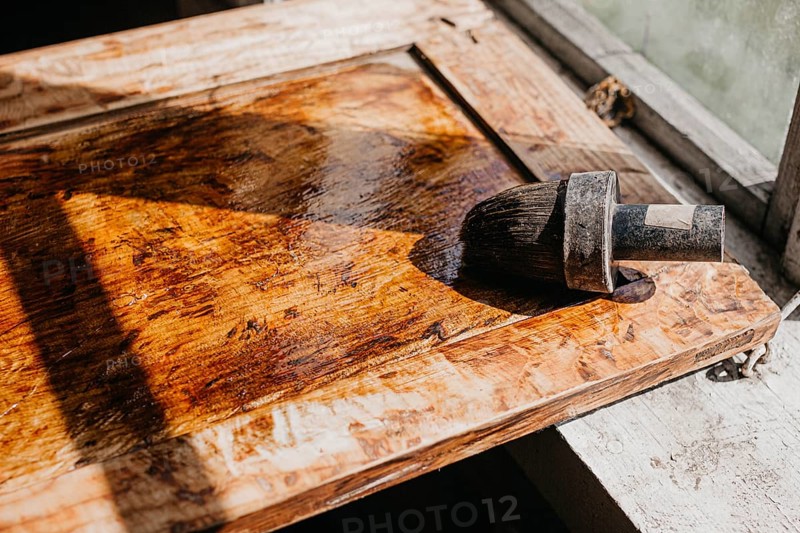 Varnished wooden surface under sunlight, highlighting texture with brush nearby