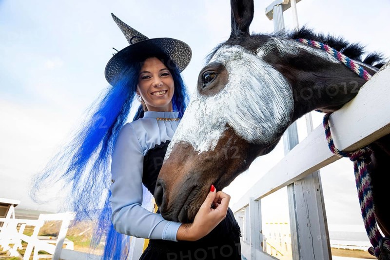 A girl dressed as a witch stands next to a horse on which a skeleton is drawn for the celebration of Halloween