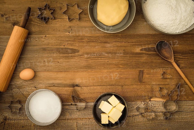 Collection of ingredients and utensils for baking Christmas biscuits with text space in the centre of the picture on a dark wooden background