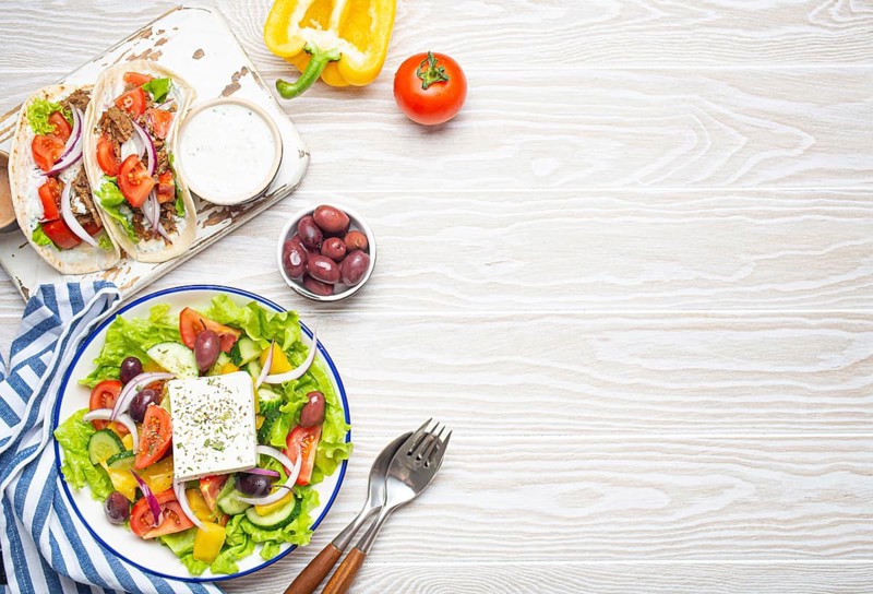 Traditional Greek Food: Greek Salad, Gyros with meat and vegetables, Tzatziki sauce, Olives on White rustic wooden table background from above. Cuisine of Greece. Copy space, food photography, food photography