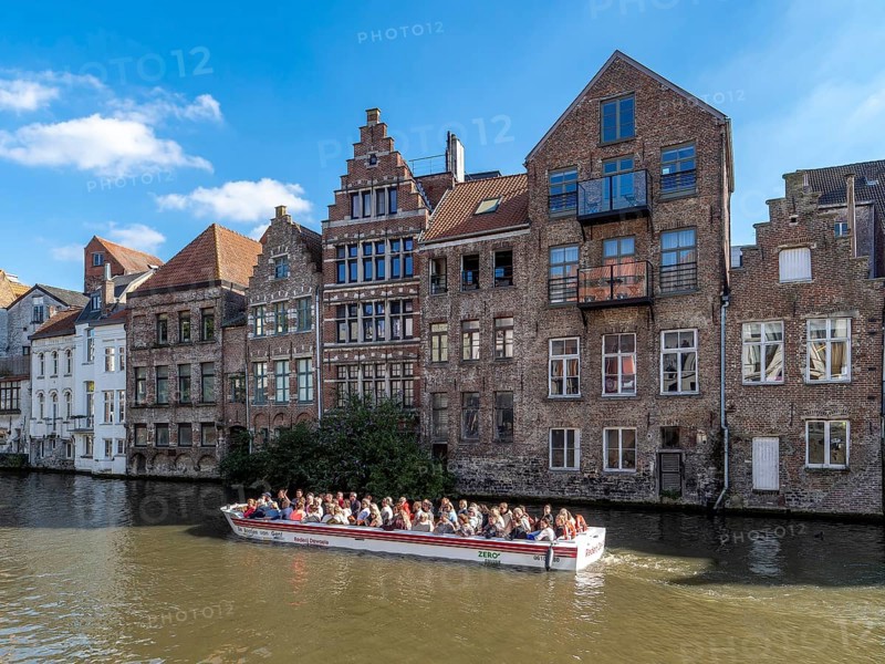 Tourists in the tourist boat for the canal cruise on the river Leie and in the background together indebted medieval historic buildings in the medieval city centre, Ghent, East Flanders, Belgium, Europe