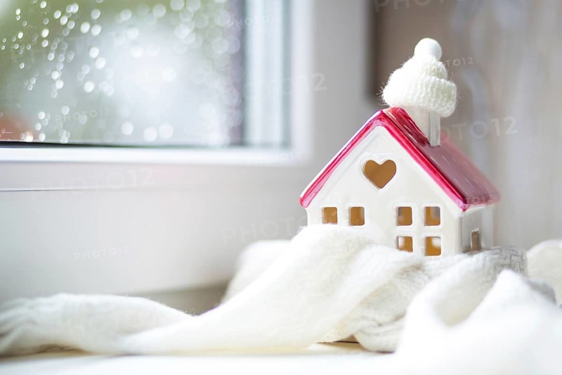 Cozy house is wrapped in a hat and scarf in a snowstorm -window sill decor. Winter, snow, home insulation, protection from cold and bad weather, room heating system. Festive mood, Christmas, New Year