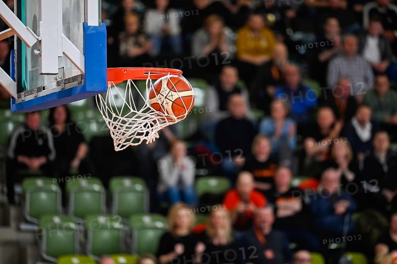 Ball falls in the basket during basketball match. Audience in the background.
