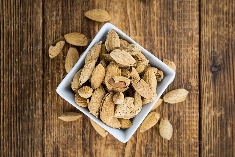 Roasted Almonds (in shell) on an old wooden table (close-up shot, selective focus)