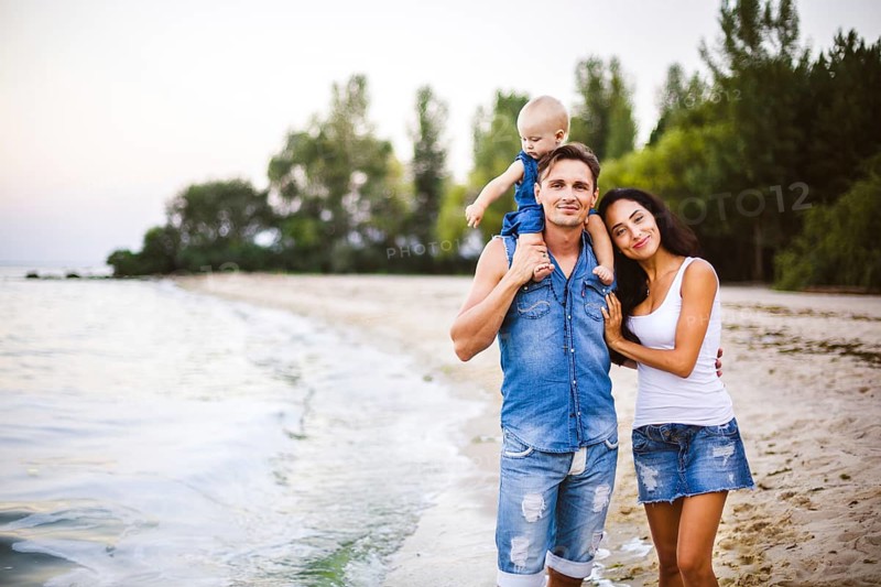 Beautiful young family on holiday with baby. The father holds the blonde girl in her arms, and the brunette's mother hugs her husband. The concept of a family beach holiday summer near the sea
