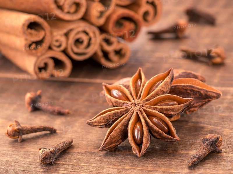 Star anise on wooden background close up. Blurred clove and cinnamon sticks as background