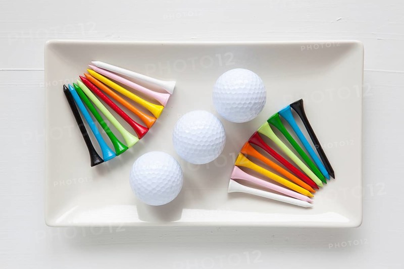 White ceramic dishes with golf balls and wooden tees on over white background, rectangle dish