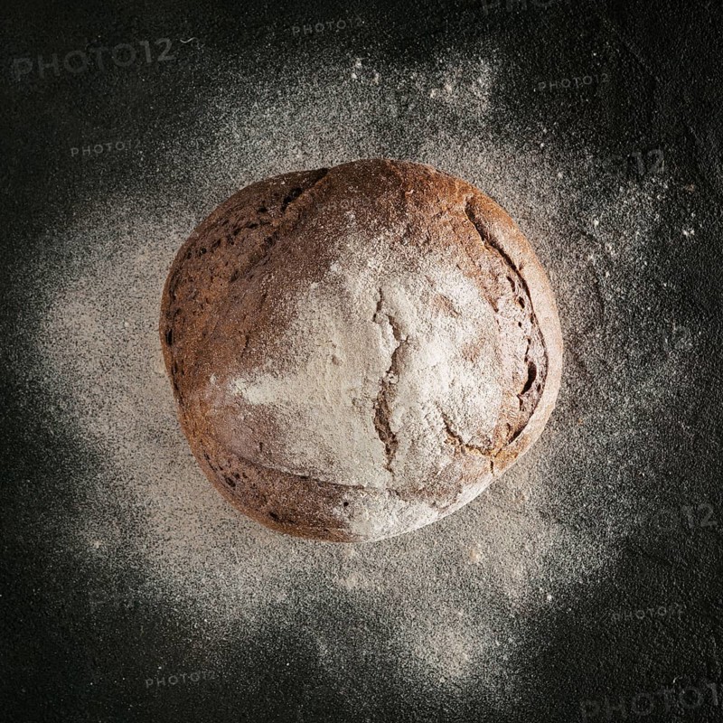 Whole homemade rye bread with rye flour on black textured background. Top view or flat-lay. Low key