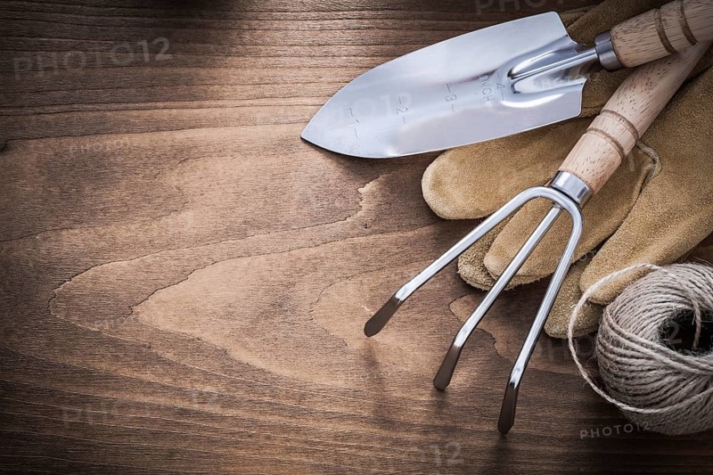 Metal hand spade rake brown leather gardening gloves and hank of string on vintage wood board agriculture concept