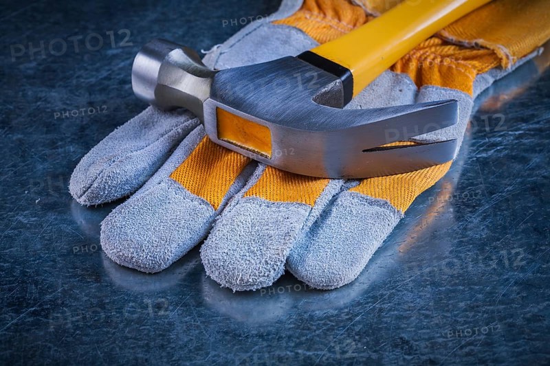 Safety gloves with claw hammer on scratched metallic background construction concept