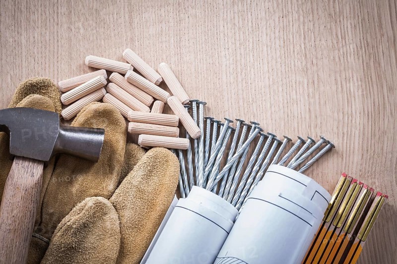 Collection of wooden meter dowels construction drawings claw hammer leather safety gloves and steel nails on wood board maintenance concept